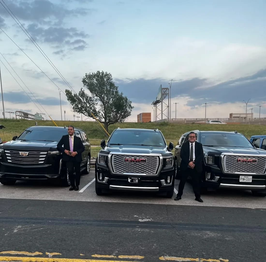 Two Leo Limos chauffeurs in tailored suits beside a Cadillac Escalade and GMC Yukon Denali